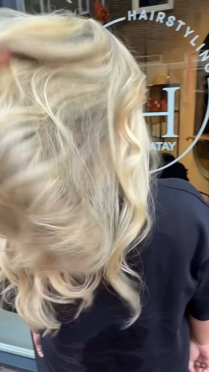 Blond golvend haar voor het salonraam met het MH-logo